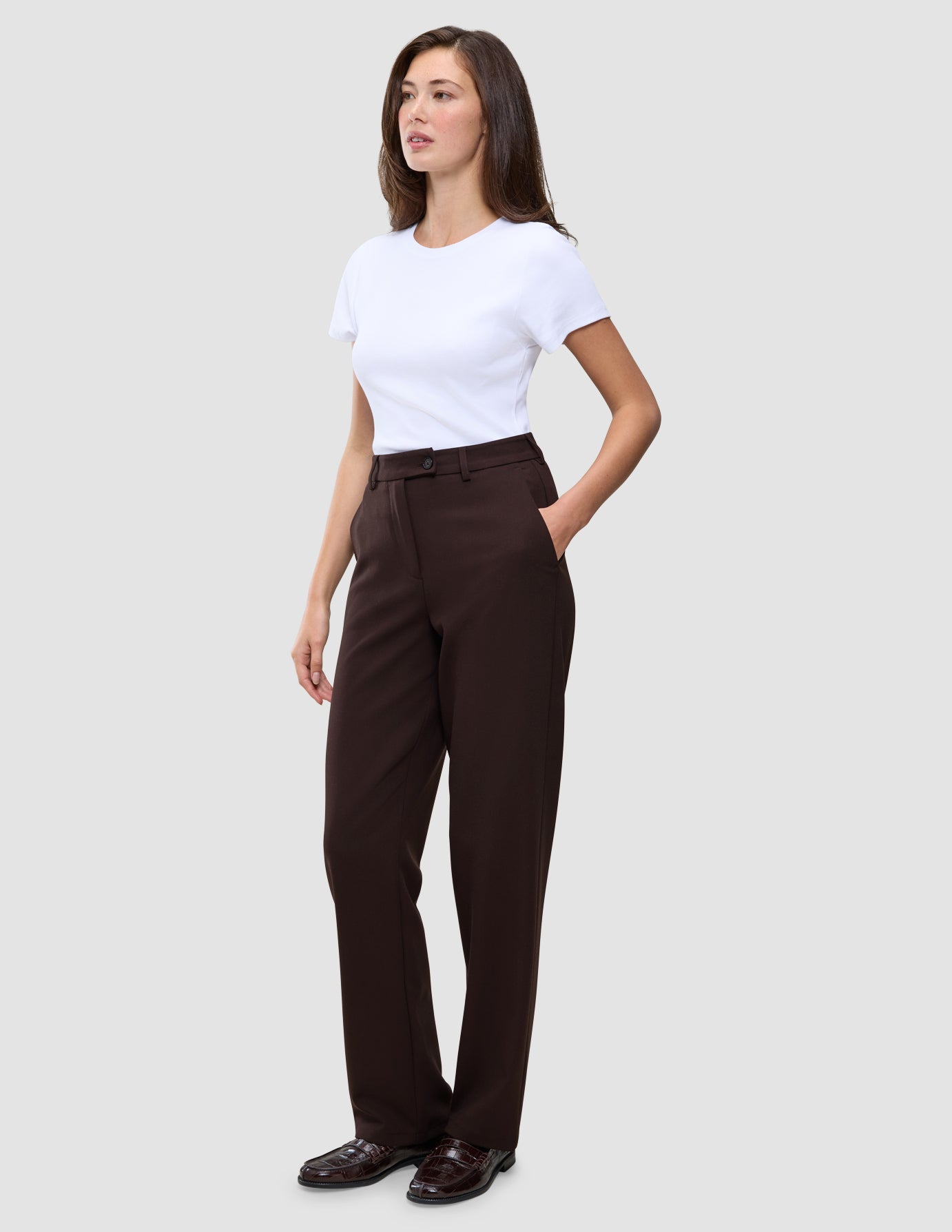En kvinna klädd i en vit t-shirt och ett par Women GO2 Pants Straight Mocha med raka ben, med handen i fickan.
